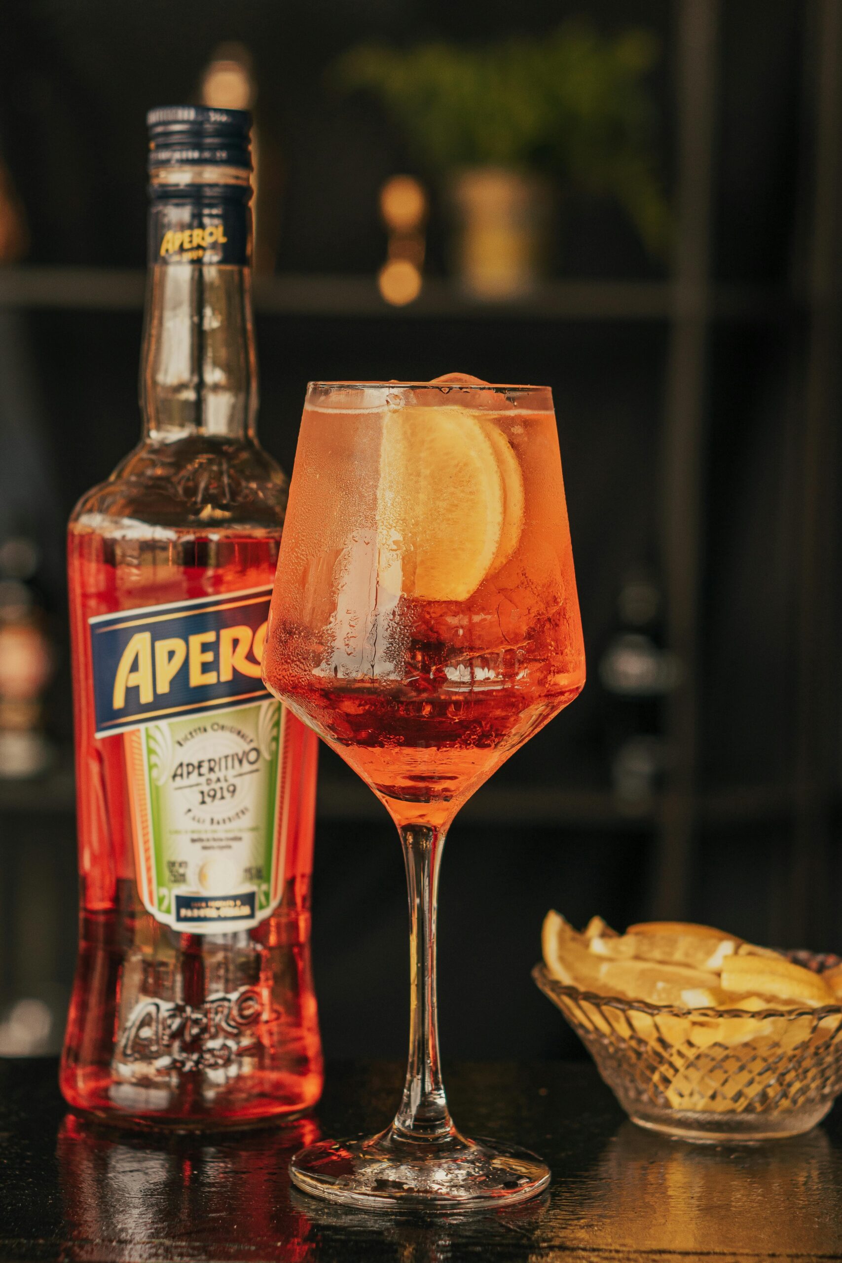 Close-up of a classic Aperol Spritz with orange slice, featuring Aperol bottle and lemon wedges.