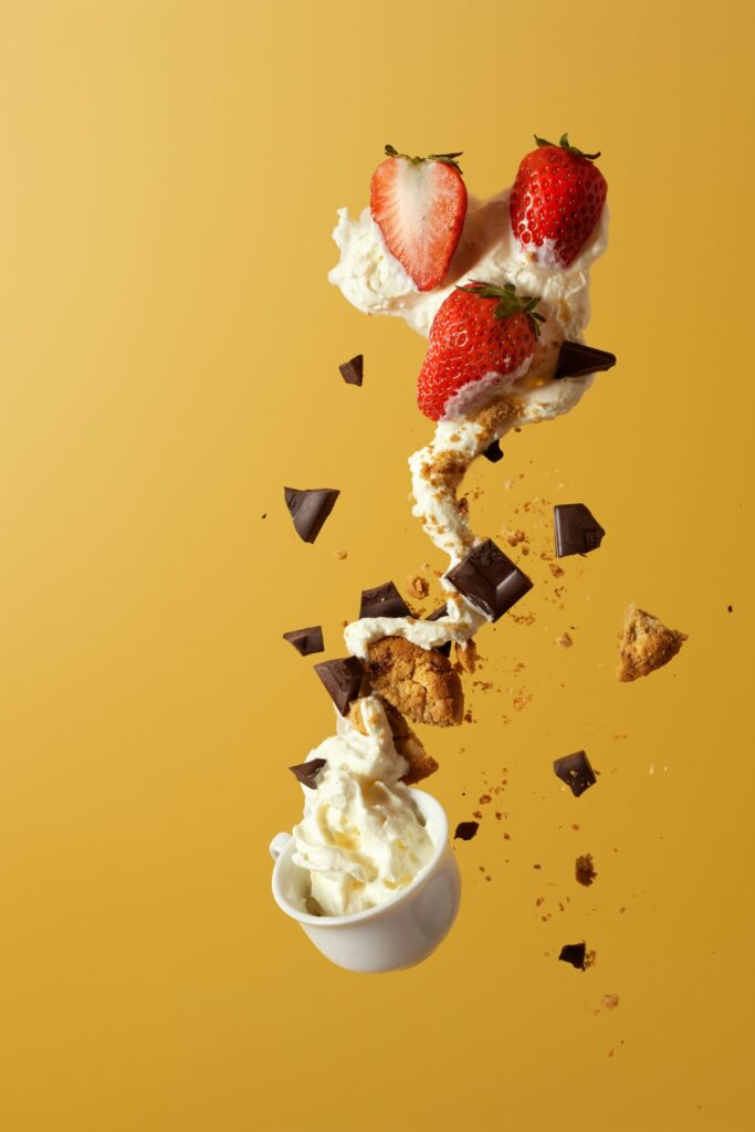 Delicious strawberries and cream with chocolate and cookie pieces, captured in mid-air against a vibrant yellow background.