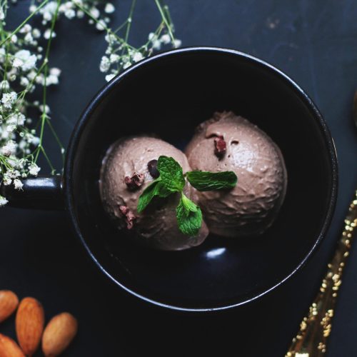Delicious chocolate ice cream in a bowl garnished with mint leaves and almonds.